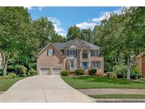 Charming two-story brick home with a two-car garage, lush landscaping, and a curved driveway at 1625 Hawkins Cove Trl, Roswell, GA 30076
