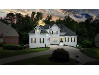 Beautiful white home featuring manicured lawns, a circular driveway, and mature trees under a colorful sunset at 6017 Chestatee Creek Nw Ct, Acworth, GA 30101