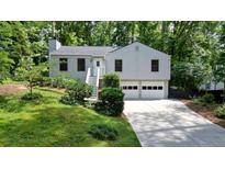Charming home with manicured lawn, inviting entryway stairs, and two-car garage nestled among mature trees at 7025 Stone Wood Nw Dr, Kennesaw, GA 30152