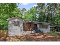 Charming white brick home with modern wood accents, black trim, and mature trees at 2238 Pinecliff Ne Dr, Atlanta, GA 30345