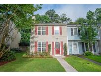 Charming townhome featuring a well-manicured lawn, mature trees, and inviting red door with matching window shutters at 3053 Shadow Walk Ln, Tucker, GA 30084