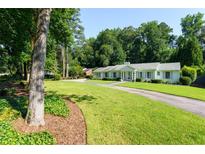 Expansive front yard featuring a long driveway leading to a well-maintained, light colored ranch-style home surrounded by mature trees at 4095 N Broadland Nw Rd, Atlanta, GA 30342