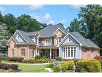 Attractive brick and blue paneled two-story home with manicured lawn, garden beds, and mature shade trees at 217 Fernwood Pl, Woodstock, GA 30188