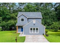 Charming two-story home featuring a blue exterior, a well-manicured lawn, and a paved driveway, set among lush green trees at 597 Woodcrest Manor Dr, Stone Mountain, GA 30083