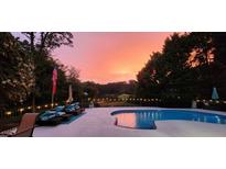 Backyard pool at sunset features patio furniture, string lights, and a beautiful view of trees and the lake beyond at 5286 Wild Indigo Nw Way, Acworth, GA 30102
