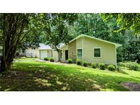 Charming single-story home featuring a stone accent wall, lawn, and a backdrop of lush trees at 3900 Ferncliff Rd, Snellville, GA 30039