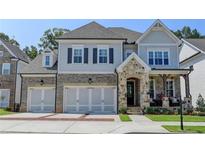Charming two-story home featuring a stone and brick facade, three-car garage, and inviting front porch at 11255 Knollwood Bnd, Johns Creek, GA 30097