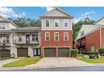 Charming townhome featuring a brick facade and individual garages, set against a backdrop of mature trees at 5933 Brookside Oak Cir, Norcross, GA 30093