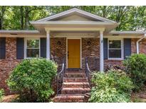 Charming brick home featuring a bright yellow front door, perfect landscaping, and covered porch at 1393 Sagewood Cir, Stone Mountain, GA 30083