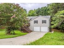 Charming home featuring a two-car garage, inviting staircase, and blossoming tree in a lush, green lawn at 49 Sweetwater Ct, Powder Springs, GA 30127