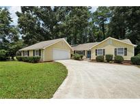 Charming yellow home featuring an attached garage, well-maintained lawn, and lengthy driveway at 2466 Country Club Dr, Conyers, GA 30013