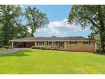 Ranch-style home with a brick facade, manicured lawn, and mature trees on a sunny day at 3212 Georgian Woods Cir, Decatur, GA 30034