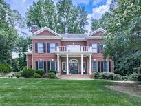 Charming brick home boasts a covered front porch, balcony, manicured lawn, and mature landscaping at 4450 Barony Dr, Suwanee, GA 30024