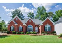 Charming red brick home with a manicured lawn, decorative windows, and lush landscaping at 205 Finsbury Park Ct, Suwanee, GA 30024