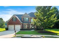 Charming two-story brick home featuring lush landscaping, a two-car garage, and a welcoming front porch at 1496 Clarecastle Ln, Buford, GA 30519