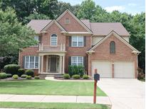Charming two-story brick home featuring a well-manicured lawn, mature trees, and a two-car garage at 5157 Wellisford Ct, Suwanee, GA 30024