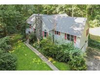 Charming home exterior featuring a stone chimney, red shutters, and lush landscaping in a wooded setting at 1252 Grist Mill Dr, Acworth, GA 30101