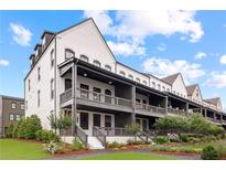 View of townhomes with covered front porches and landscaped lawns against a blue sky with clouds at 6710 Pippin Walk, Alpharetta, GA 30005