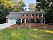 Charming two-story brick home featuring a manicured lawn, attached garage, and classic black shutters at 3375 Rivendell Ct, Roswell, GA 30075