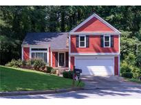 Charming two-story red home featuring a well-maintained lawn, white garage door, and black window shutters at 7472 Woods Ct, Lithonia, GA 30248