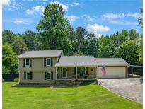 Charming two-story home featuring a metal roof, cozy front porch, and attached two car garage, surrounded by lush trees at 2081 Old Peachtree Road Northeast Rd, Lawrenceville, GA 30043
