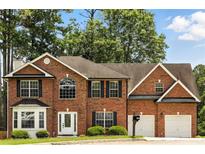 Charming two-story red brick home with a two-car garage, manicured landscaping, and mature trees at 5745 Crystal Springs Way, Powder Springs, GA 30127