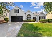 Charming white brick home featuring a lush green lawn, manicured shrubs and a black garage door at 3208 Spruce Way, Atlanta, GA 30349