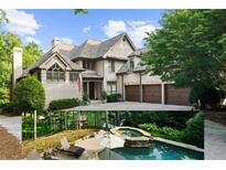 Elegant exterior featuring a three-car garage, white brick, and a stone chimney with a paved driveway and mature trees at 1525 Lockridge Dr, Cumming, GA 30041