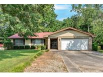 Charming single-story home with mature trees, lush lawn, two-car garage, and a brick and siding exterior at 4866 S Lilburn Stone Mountain Road Sw Rd, Lilburn, GA 30047