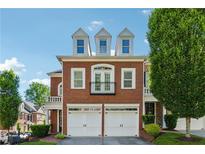 Charming brick townhome with a two-car garage and dormer windows under a clear blue sky at 11715 Dancliff Trce, Alpharetta, GA 30009