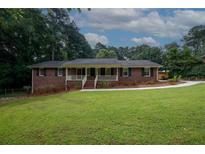 Charming brick home featuring a welcoming front porch, lush green lawn, and mature trees creating a serene setting at 2202 Springdale Dr, Snellville, GA 30078