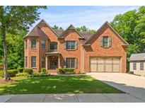 Elegant brick home with a well-manicured lawn, lush greenery, and attached two-car garage at 1170 Shellnut Trl, Hoschton, GA 30548