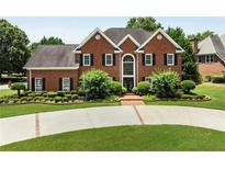 Stately brick home featuring a well manicured lawn, dark shutters, and a circular driveway at 6310 Buckingham Pl, Cumming, GA 30040