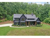 Stunning dark modern farmhouse with inviting front porch and lush lawn with a beautiful wooded backdrop at 2100 Mountain Cove Ct, Woodstock, GA 30188