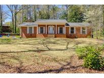 Charming brick home featuring a covered porch, white columns and shutters, and a spacious front lawn at 6339 Cornelia Dr, Douglasville, GA 30134