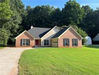 Charming brick home with manicured lawn, complemented by mature trees and a welcoming red front door at 5415 Windcrest Ln, Suwanee, GA 30024