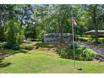 Charming single-story home with a well-manicured lawn, mature trees and American flag in a wooded setting at 506 Bolijeri Blvd, Villa Rica, GA 30180