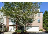 Brick townhouse featuring a two-car garage, well-maintained landscaping, and shuttered windows at 11768 Wellsley Way, Johns Creek, GA 30005