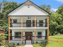 Charming two-story home featuring a double balcony, wooden support beams, and landscaped front yard at 490 Third Ave, Scottdale, GA 30079