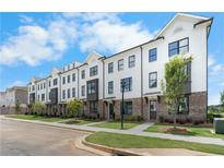 Beautiful townhome exteriors showcase white brick, black window trim, and lovely landscaping on a sunny day at 4243 Millcroft Pl # 203, Buford, GA 30518