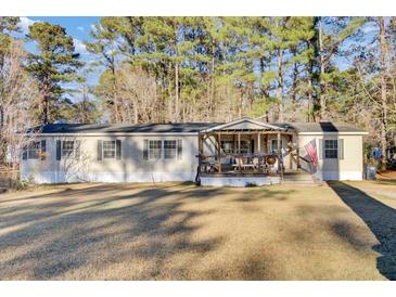 Tan mobile home with covered porch, American flag, and spacious yard at 250 W Medina St, Summerville, SC 29483