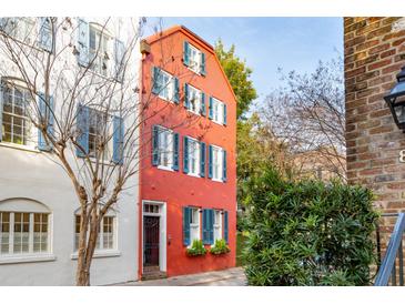 A narrow red brick home with blue shutters is flanked by white brick house and mature trees at 32 Tradd St, Charleston, SC 29401