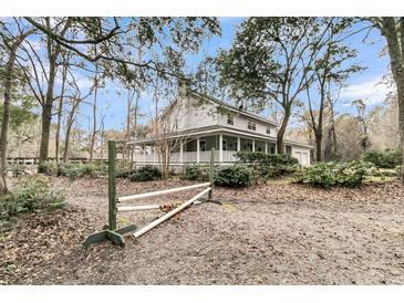 Charming two-story home with a large wrap-around porch, surrounded by mature trees and lush landscaping at 135 Rapture Ln, Wando, SC 29492