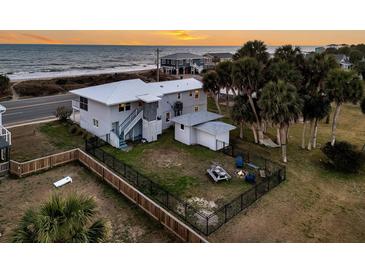 Aerial view of fenced backyard featuring a firepit, picnic table, and outdoor seating near palm trees at 407 Palmetto Blvd, Edisto Beach, SC 29438