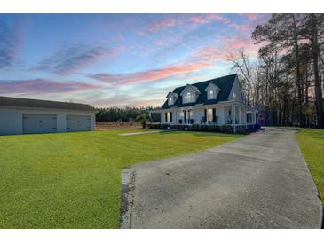 Charming home with a long driveway, a lush green lawn, and a detached garage under a colorful sunset sky at 516 & 508 Robnshers Pl, Ridgeville, SC 29472