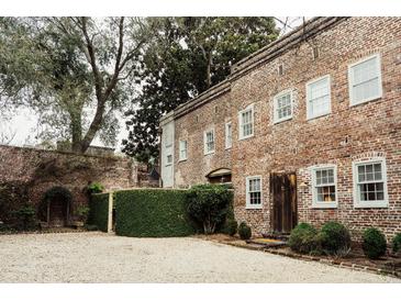 Charming brick home with a lush green landscape and gravel driveway at 42 1/2 Hasell St, Charleston, SC 29401