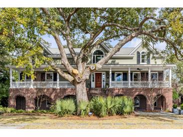 Stunning two-story home featuring a large, mature tree, covered porch, and brick facade with arched openings at 1429 Burningtree Rd, Charleston, SC 29412