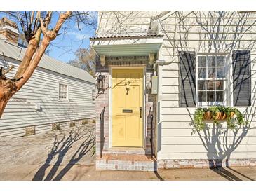 Charming home featuring a vibrant yellow front door, brick steps, and dark shutters adding character to its facade at 42 Kennedy St, Charleston, SC 29403
