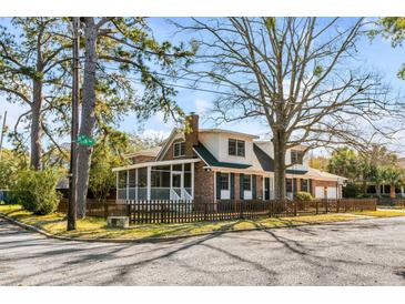 Charming two-story home featuring a screened porch, picket fence, brick accents, and mature trees at 74 6Th Ave, Charleston, SC 29403