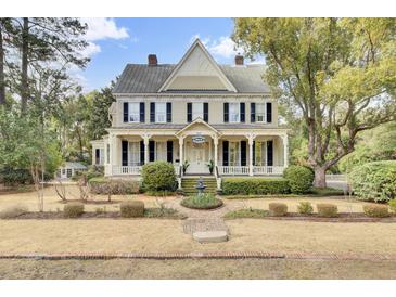 Charming two-story home featuring a welcoming front porch, black shutters, mature trees and manicured lawn at 710 S Main St, Summerville, SC 29483